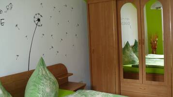 A bedroom with a green bedspread, a wooden wardrobe, and a wall with a dandelion pattern.