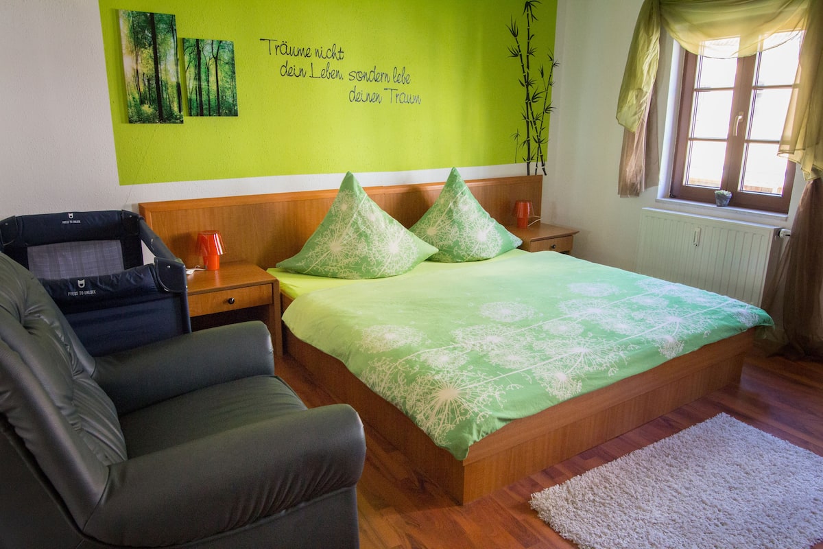 Um quarto com uma cama, uma cadeira, uma mesa de cabeceira e uma janela com cortinas.