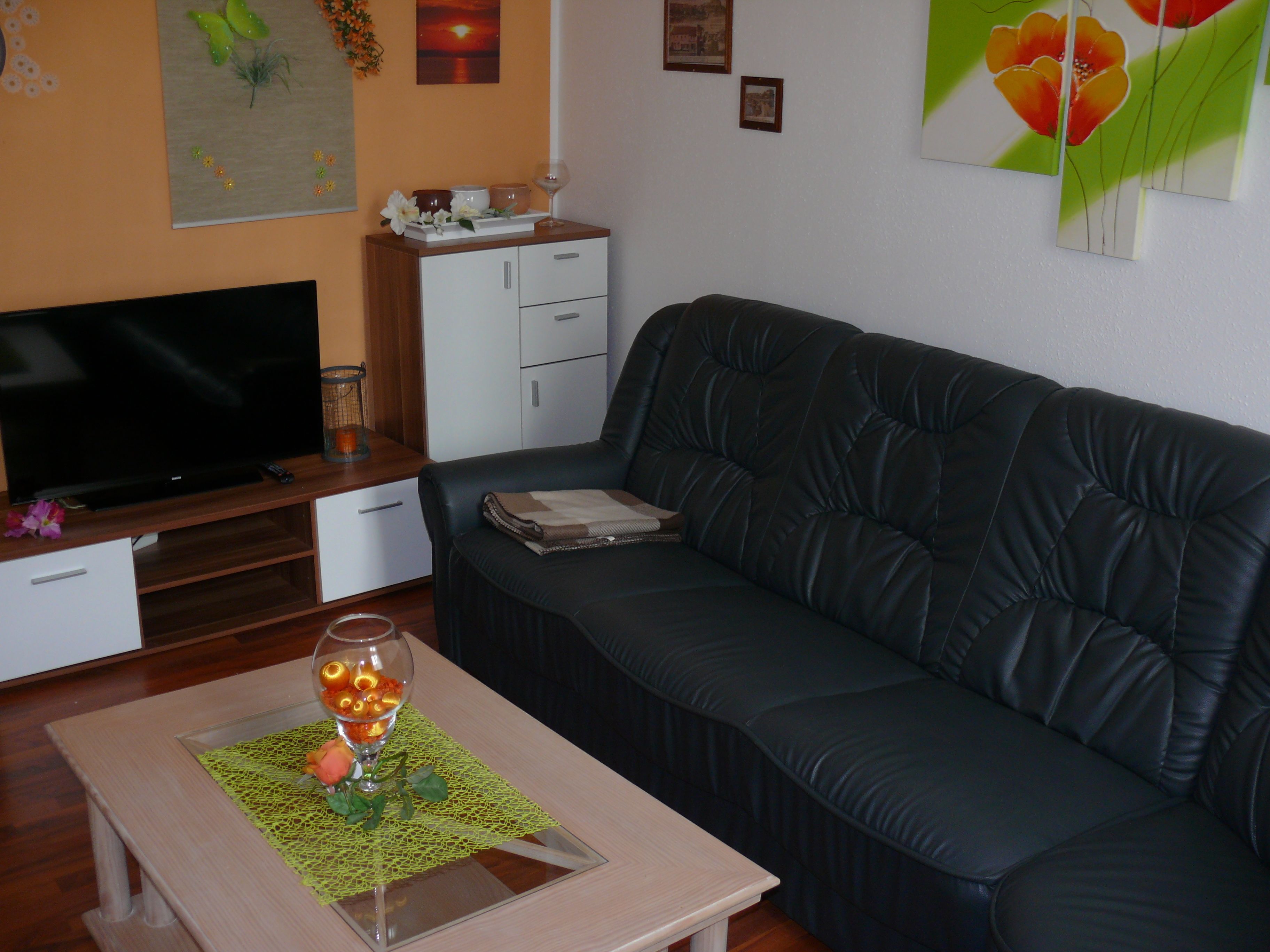 Ein Wohnzimmer mit einer Ledersofa, einem Fernseher auf einem Holzschrank und einem Couchtisch mit einer Glasvase.