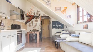 Una cocina moderna con armarios blancos, un microondas y una estufa. Hay una zona de comedor con una mesa y sillas de madera, y una sala de estar con un sofá y una mesita de centro.