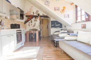 Una cocina moderna con armarios blancos, un microondas y una estufa. Hay una zona de comedor con una mesa y sillas de madera, y una sala de estar con un sofá y una mesita de centro.