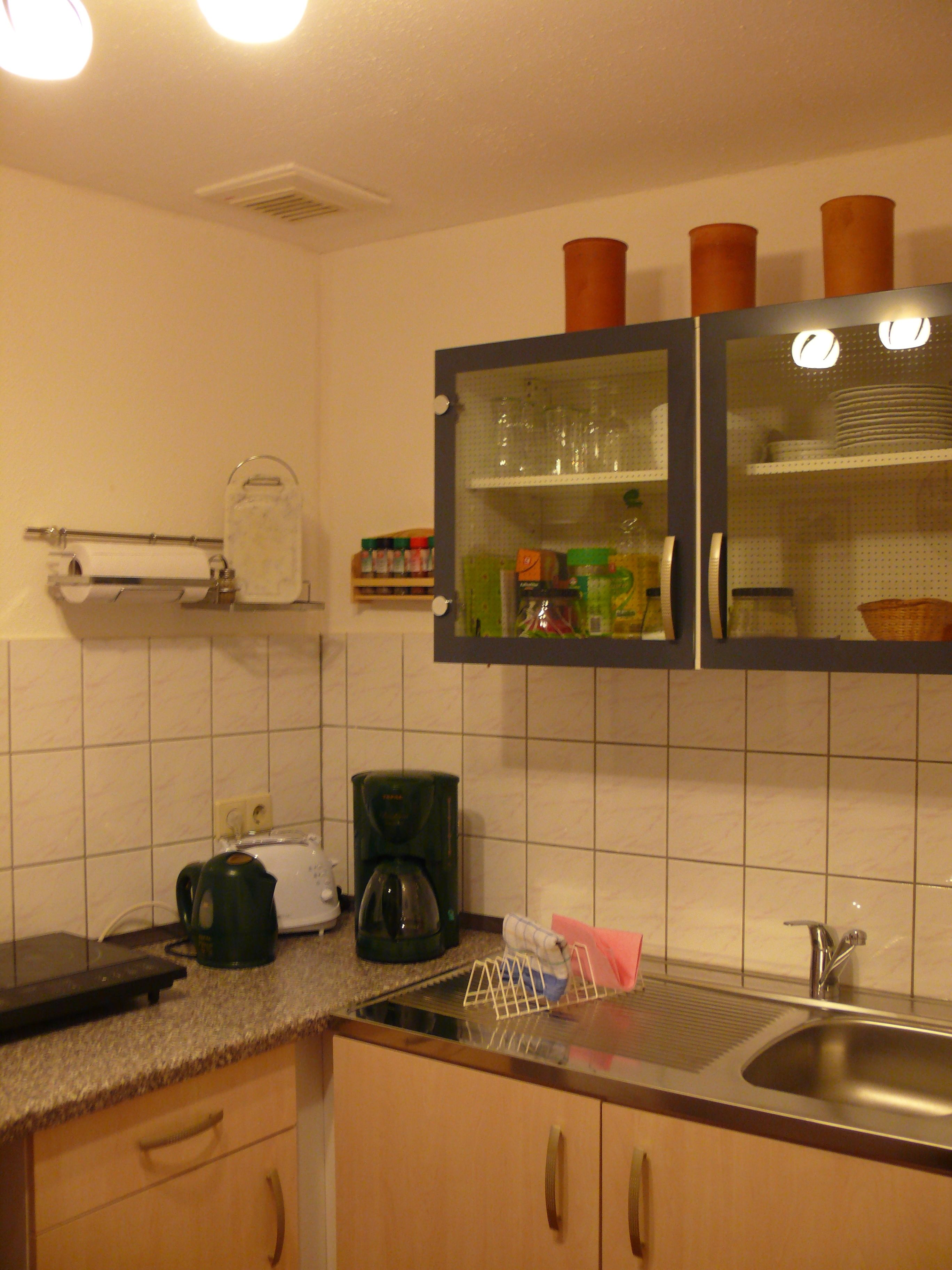 Una cocina con cafetera, lavamanos y armarios.
