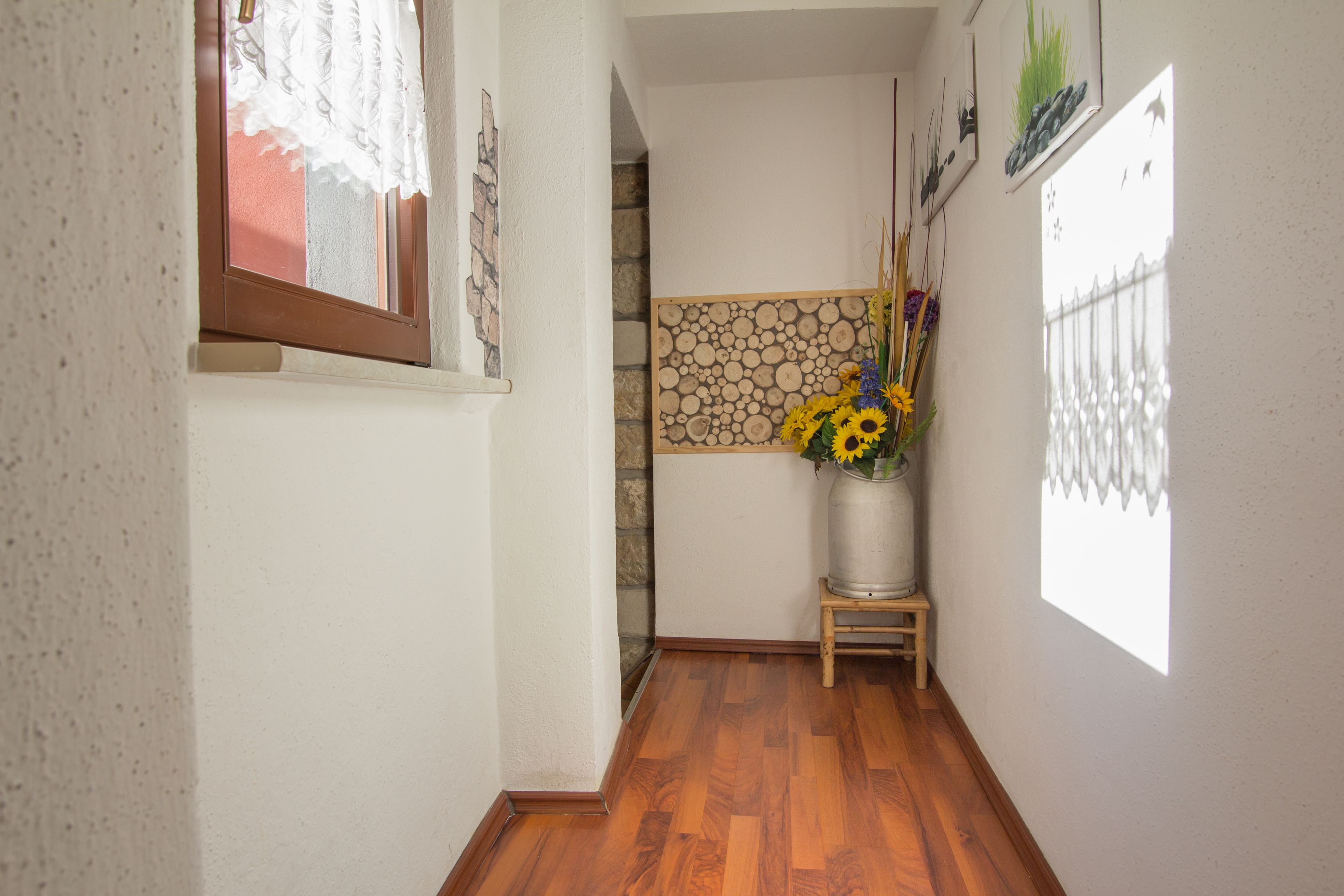 Ein Korridor mit Holzboden, einer Steinwand und einem Fenster mit Spitzenvorhängen.