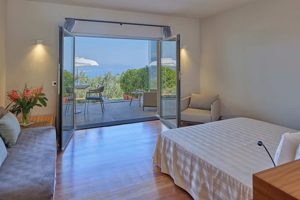 Un dormitorio con cama, sofá, mesa de comedor con sillas y balcón con vistas al mar.