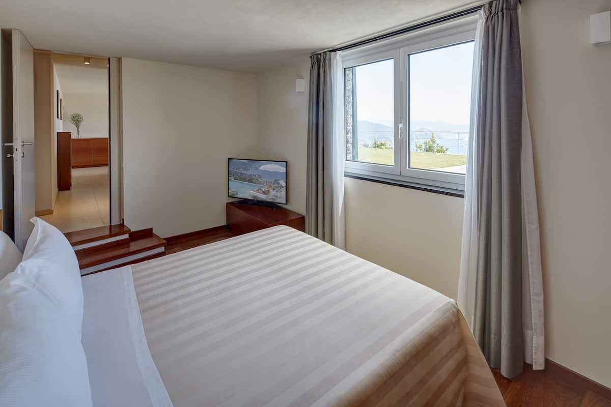 Habitación de hotel con una cama grande, un televisor en una mesita de noche de madera y una ventana con cortinas.