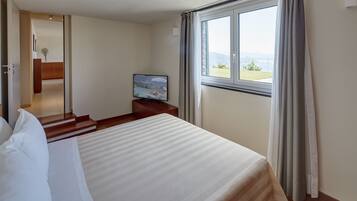 A hotel room with a large bed, a television on a wooden nightstand, and a window with curtains.