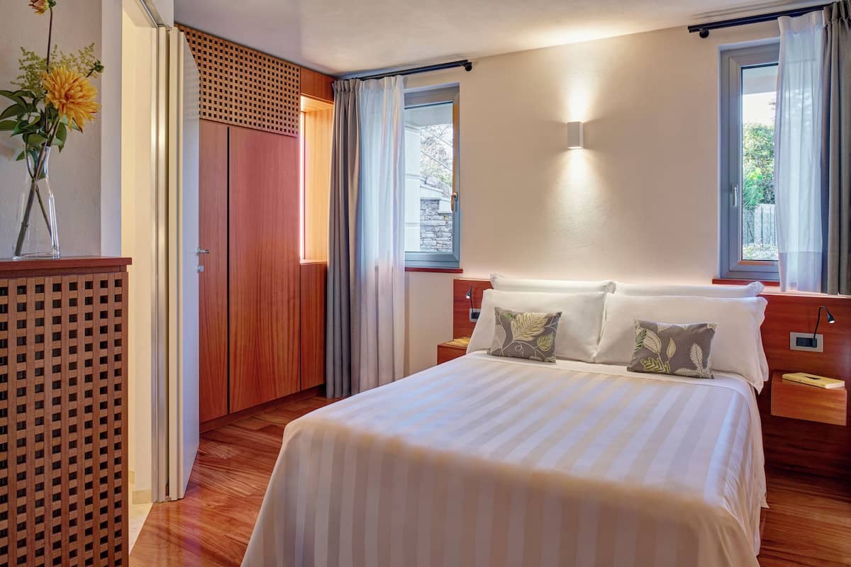 Un dormitorio ordenado con una cama grande, suelo de madera, un armario de madera y una ventana con cortinas.