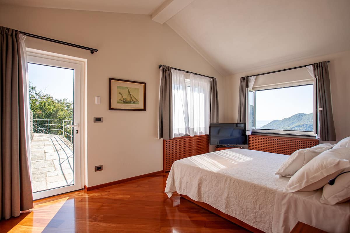 Un dormitorio con cama, televisión, ventana con cortinas y puerta que da a un área exterior.