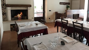 A restaurant with tables set for dining, a fireplace with logs, and a view of the outside. - Agriturismo L'Ulivo (Padula)