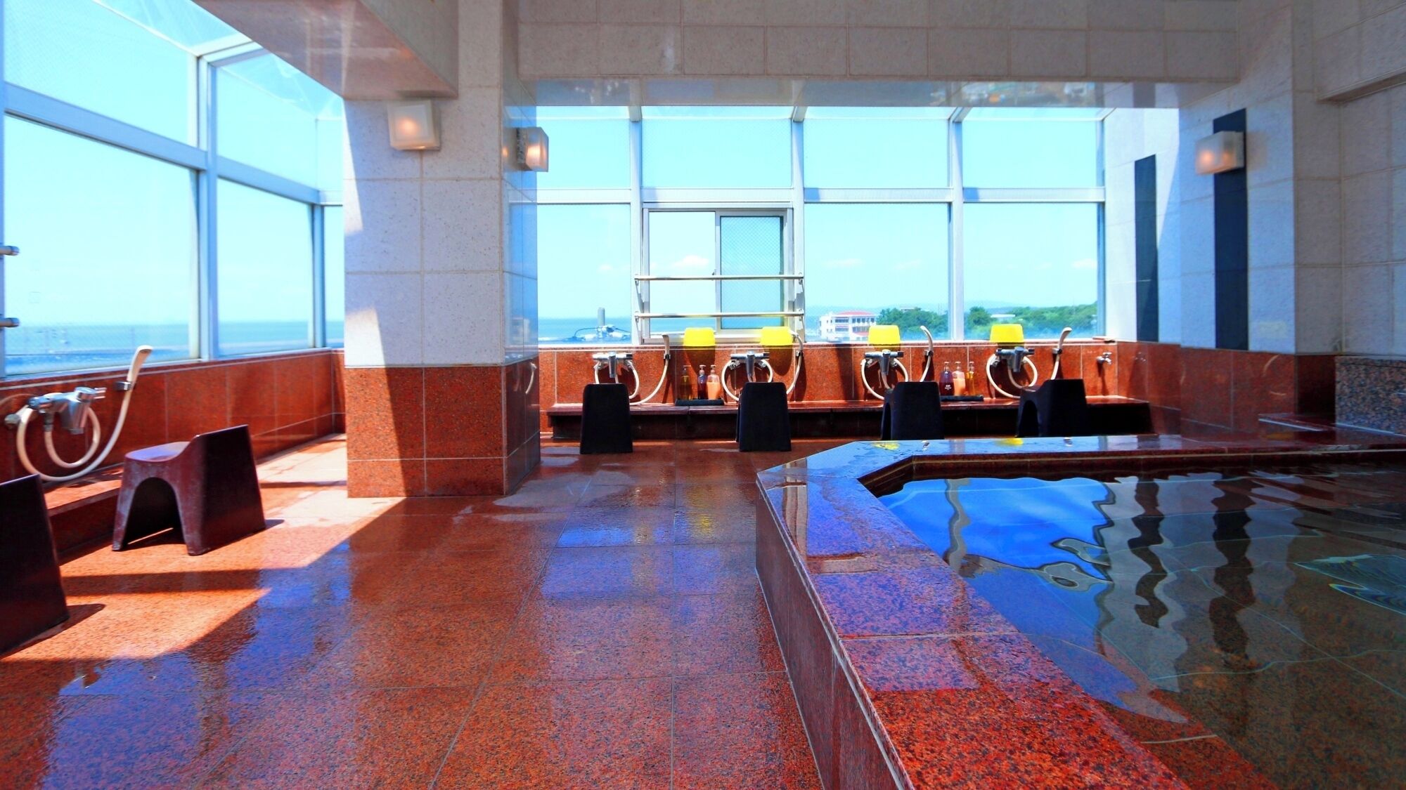 A sunlit indoor pool area with a view of the ocean, equipped with seating and a changing station.