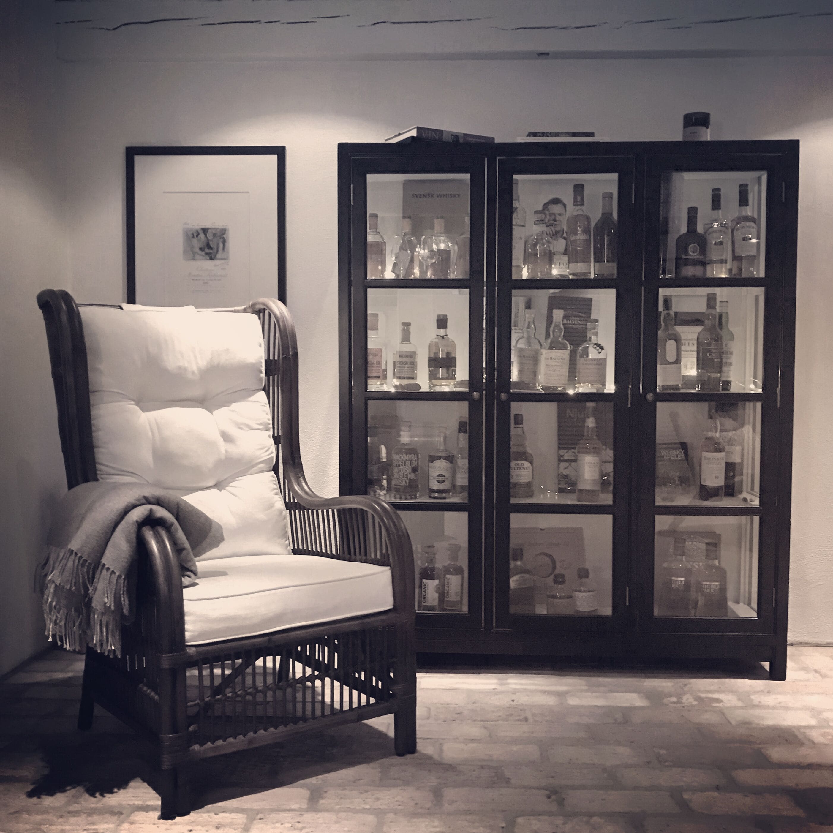 A dark wooden chair with a white cushion and a blanket, positioned in front of a glass cabinet filled with various liquor bottles.