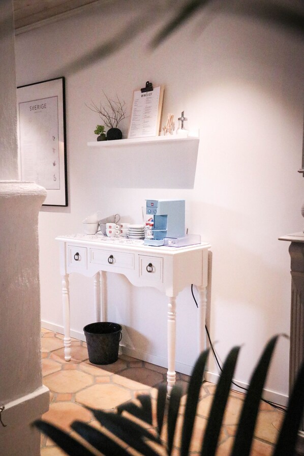 A white desk with a coffee machine, a black bucket, and a framed menu on a shelf.