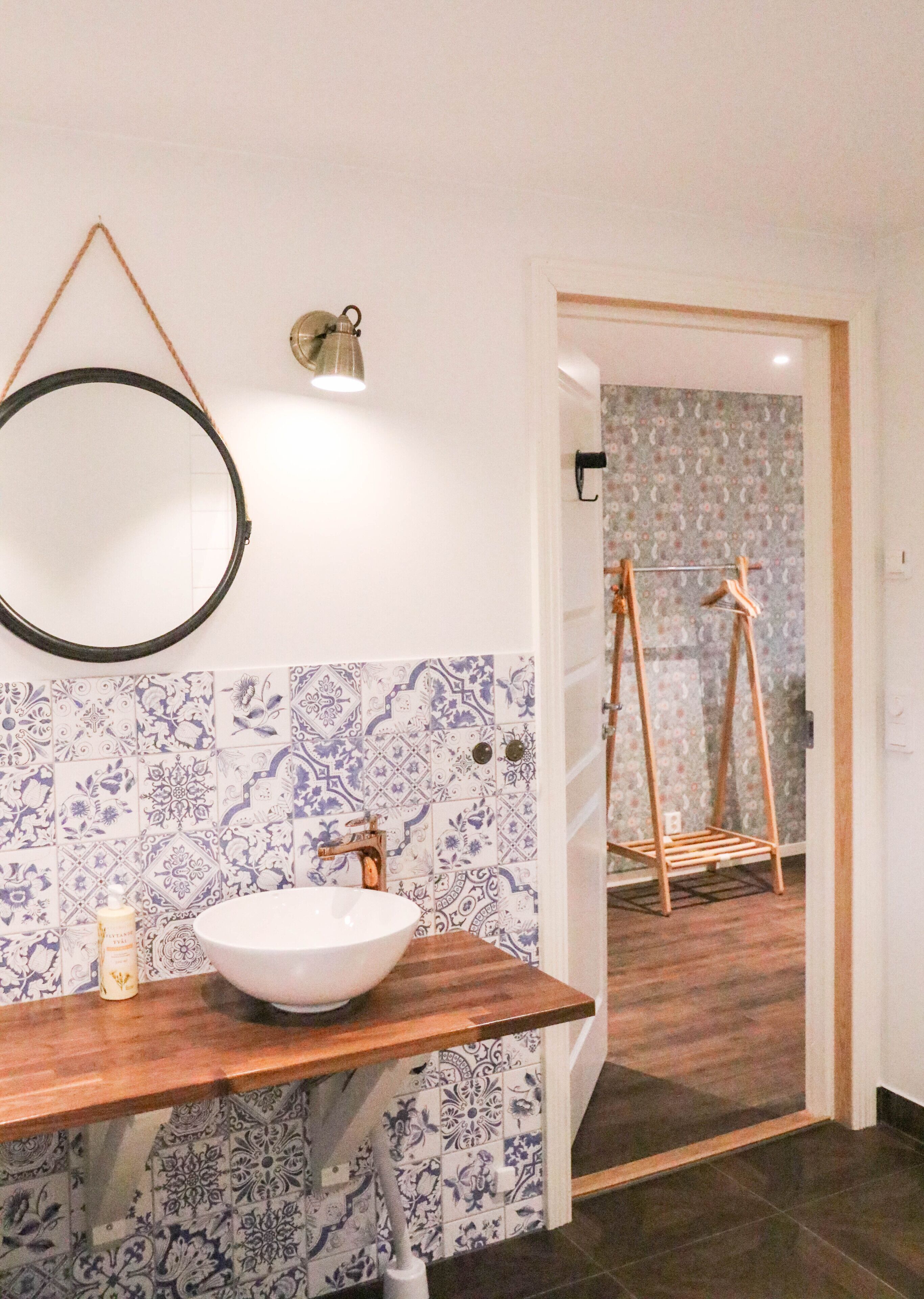 A bathroom with a wooden vanity, a round mirror, and a patterned tile backsplash.