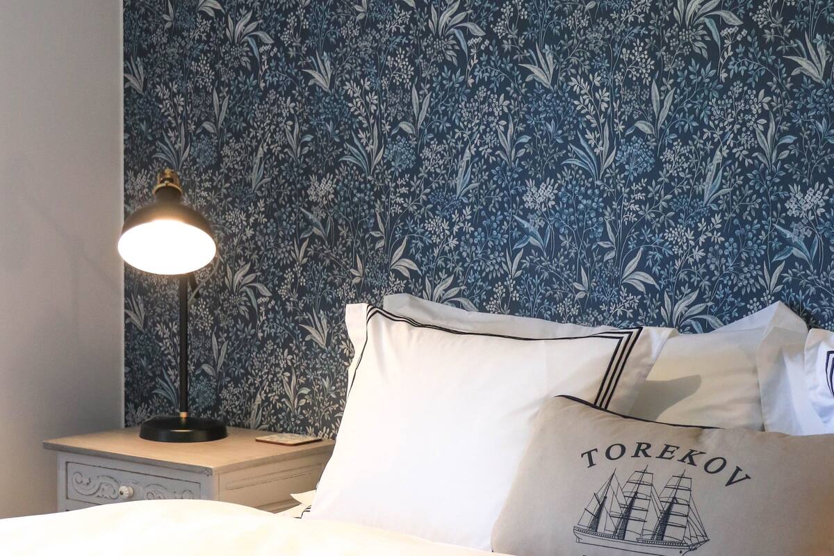 A neatly made bed with white linens, a bedside lamp, and a pillow with the text "Torekov".
