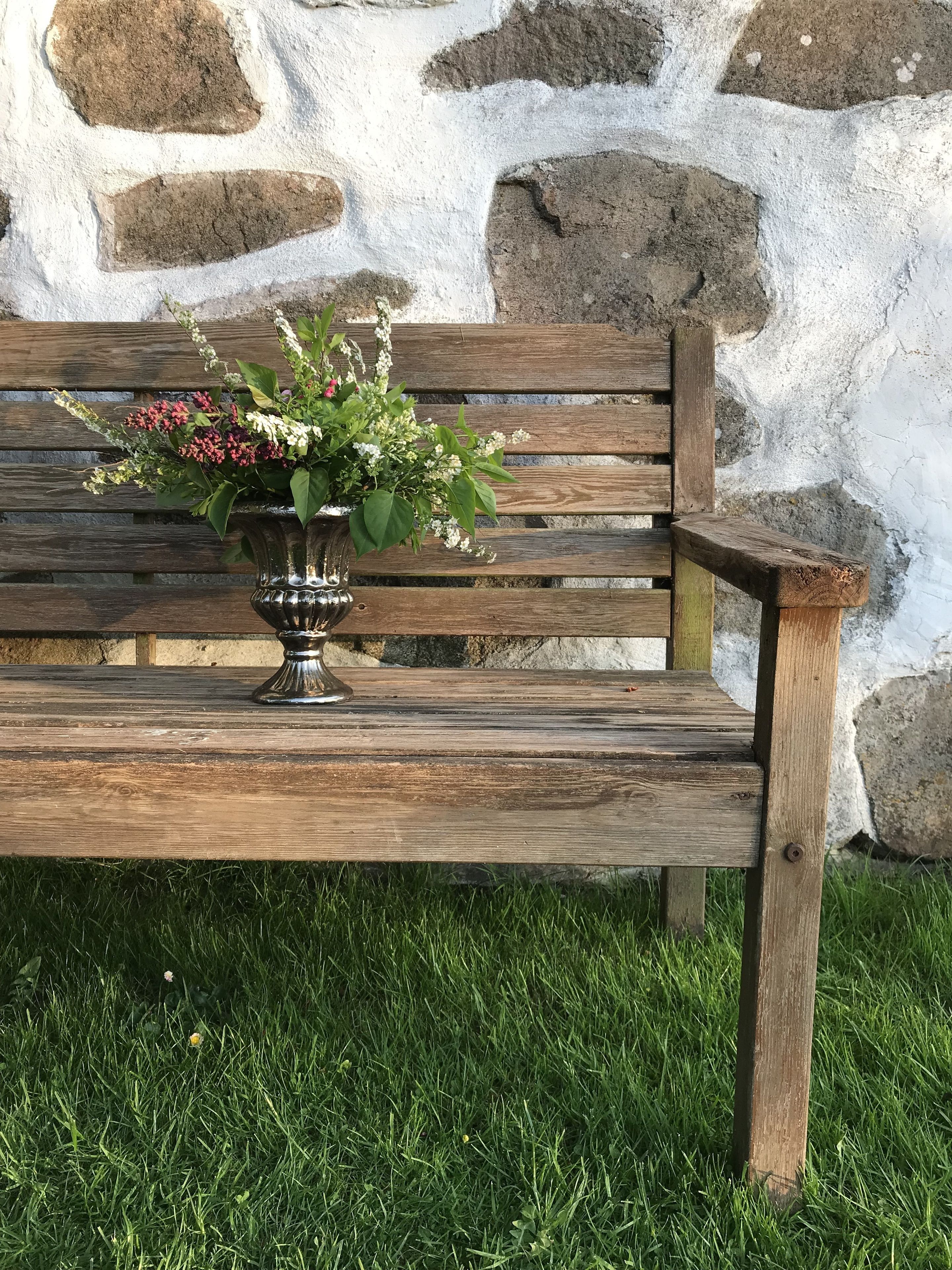A wooden bench with a metal vase containing flowers.