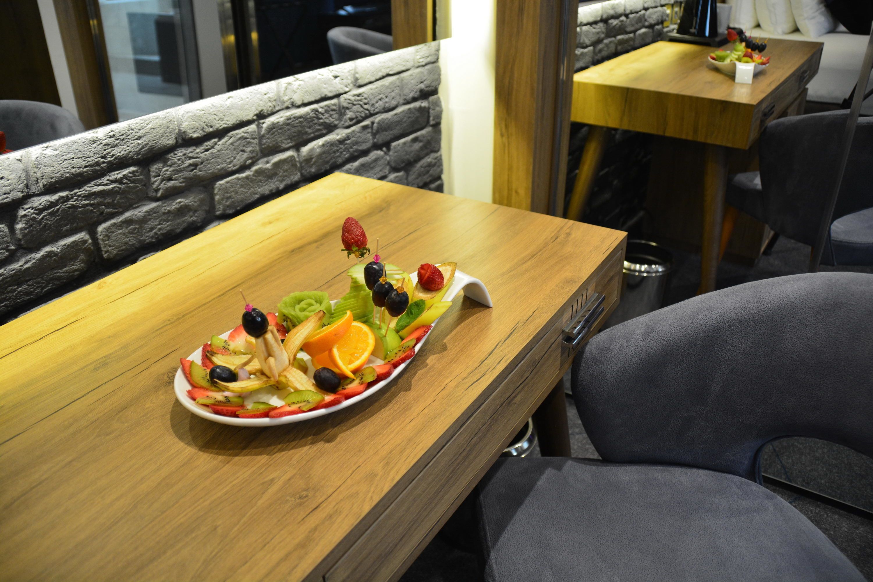 A wooden table with a fruit platter, a stone wall, and a modern chair.