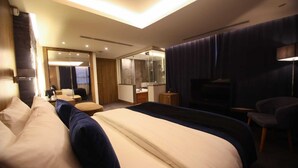 A modern hotel room with a large bed, a separate seating area, a mirror, and a television. - Monarch Hotel Amman (Amman)