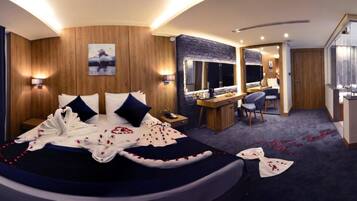 A modern hotel room with a curved bed, a desk with a chair, a television, and a large mirror.