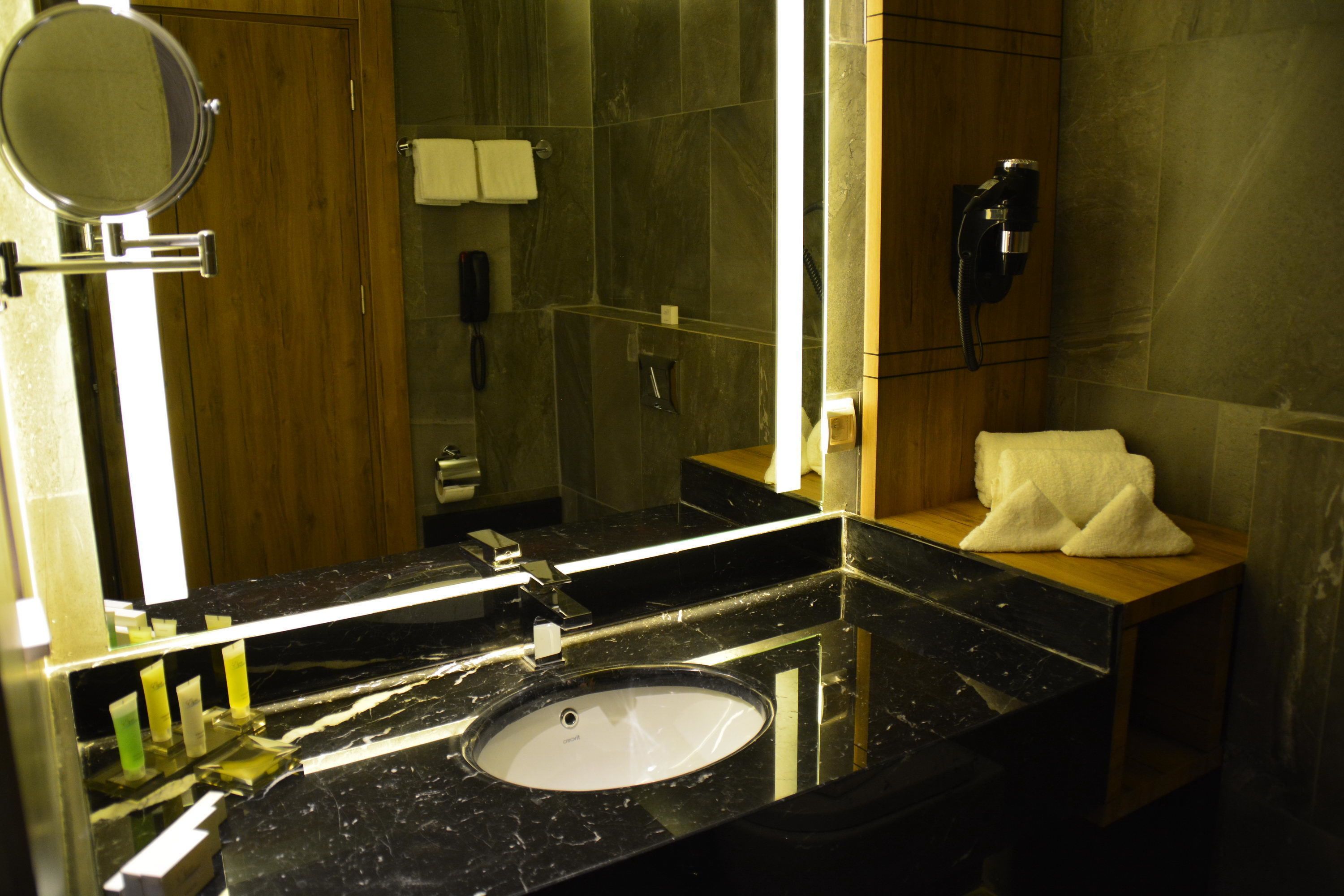 A modern bathroom with a marble sink, a round mirror, a towel rack, and a handheld showerhead.