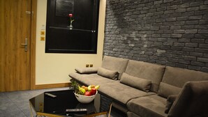 A living room with a sofa, a coffee table with a bowl of fruit, a remote control, and a brick wall. - Monarch Hotel Amman (Amman)