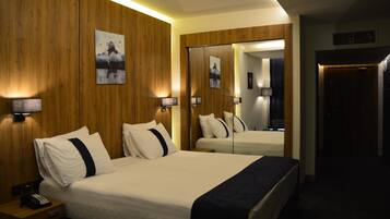 A hotel room with a large bed, bedside lamps, a wooden wall, and a mirror reflecting the room.