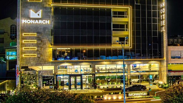 A hotel with a prominent 'MONARCH' sign, a modern glass facade, and a well-lit entrance area. - Monarch Hotel Amman (Amman)