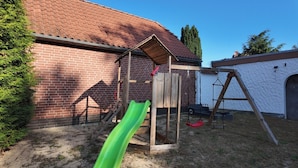 A backyard with a brick wall, a wooden play structure, a green slide, and a swing set. - Hotel Rosenhof (Bergen)