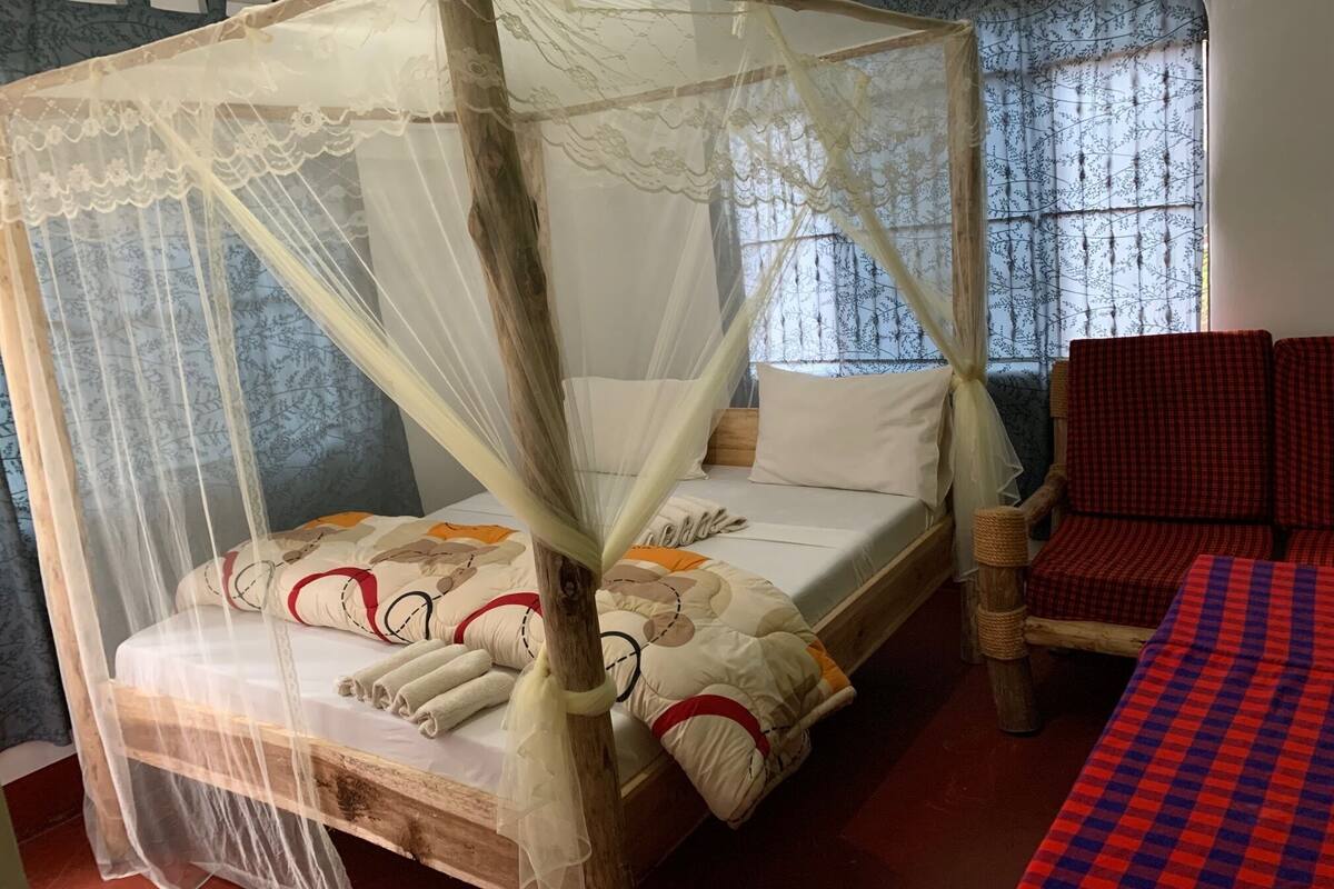 A room with a four-poster canopy bed, a wooden headboard, and a red checkered sofa.