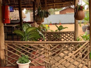A covered outdoor area with a wooden lattice fence, potted plants, and a fire extinguisher. - The Better Inn (Moshi)