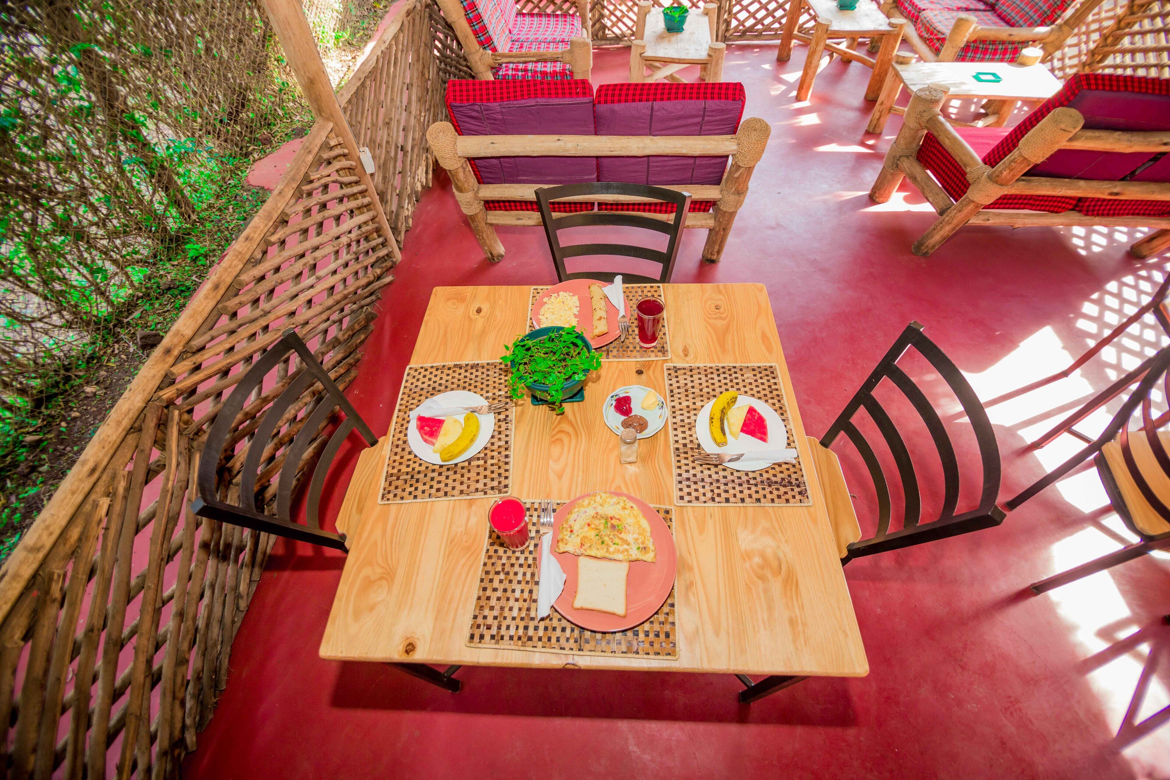 A wooden table with a red tablecloth, surrounded by wicker chairs with red cushions.