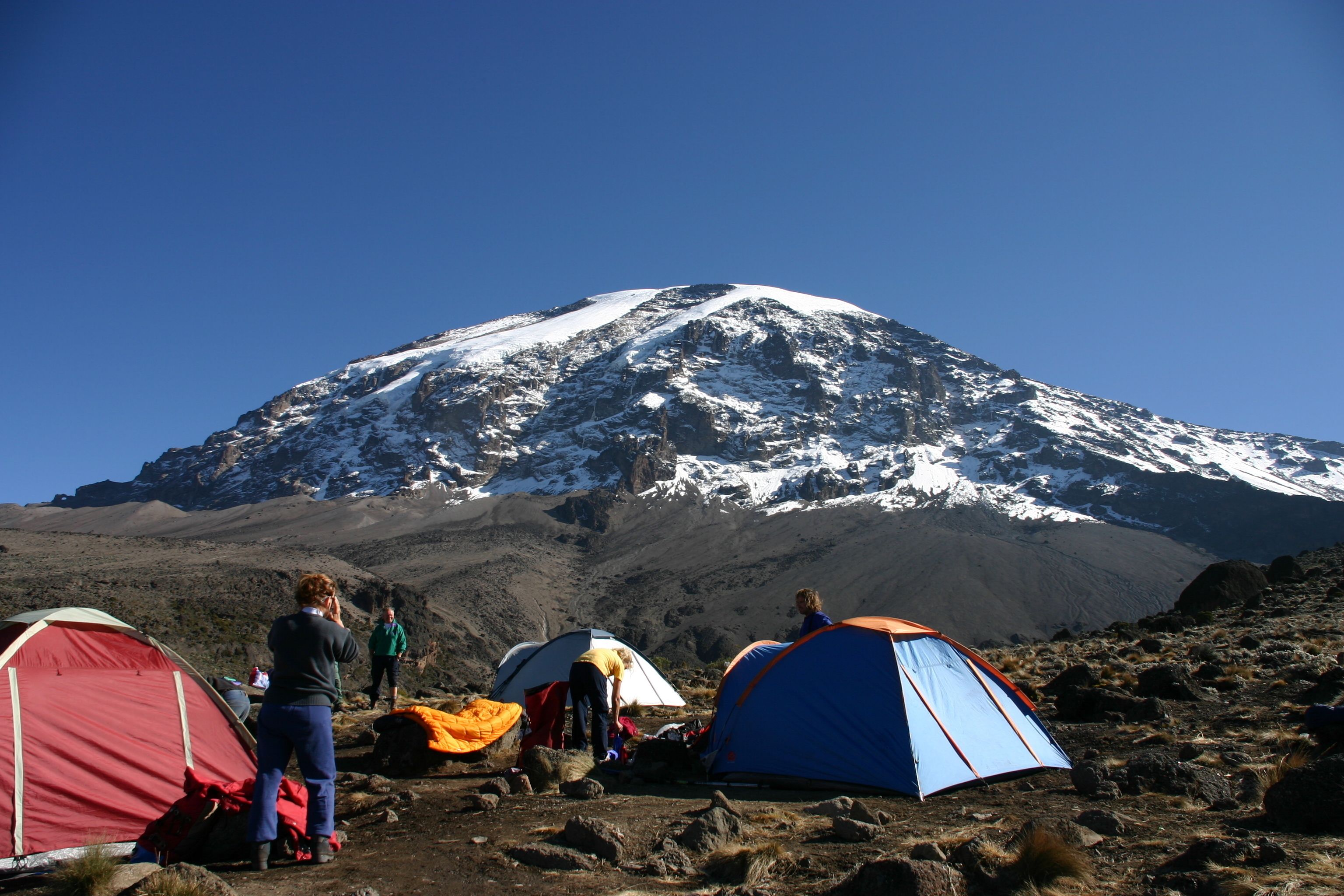 A group of tents on a rocky terrain with a snow-capped mountain in the background.