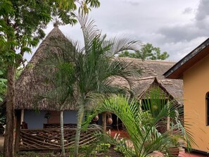 A traditional thatched-roof structure with a wooden fence and a small garden area with palm trees. - The Better Inn (Moshi)