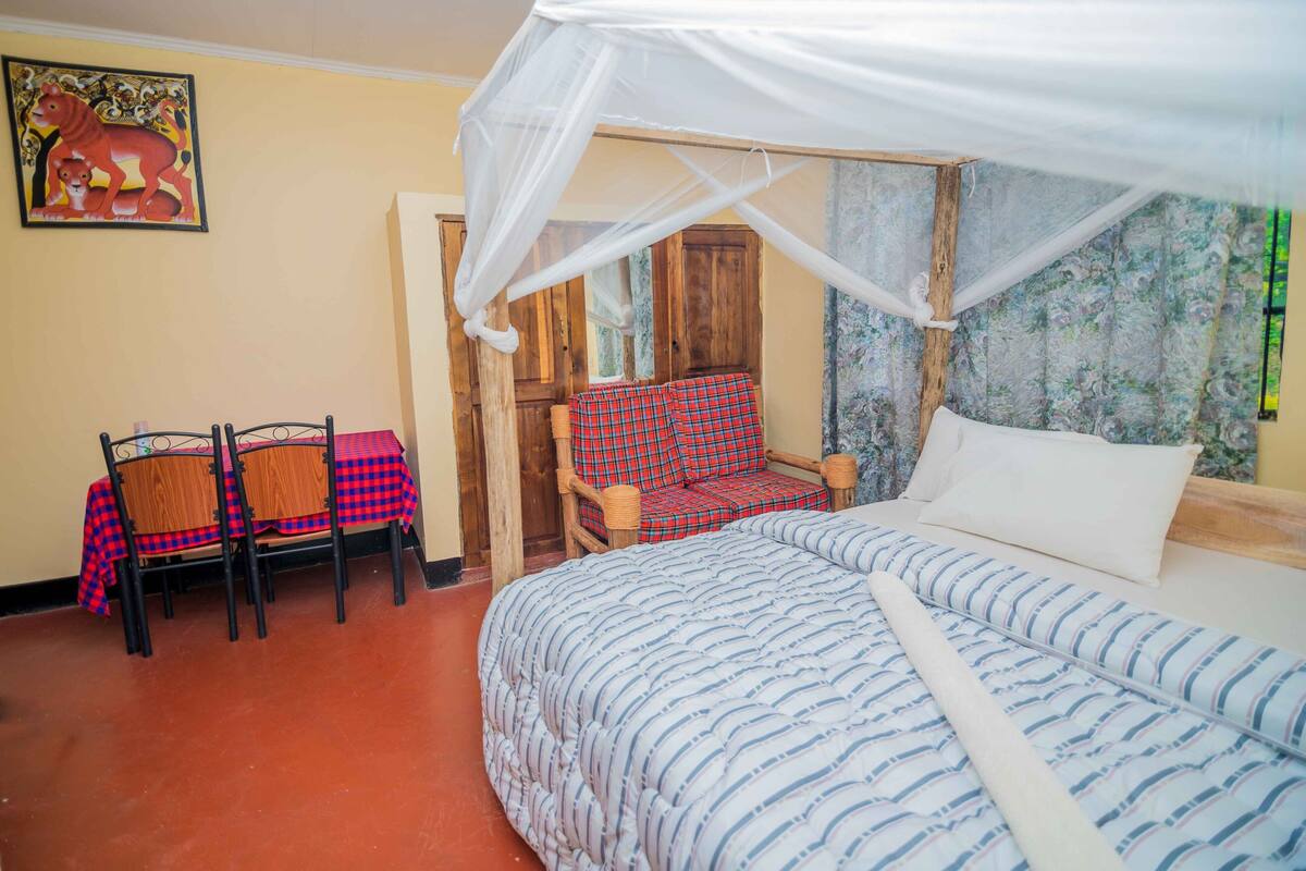 A bedroom with a bed, a chair, a table, and a mosquito net.