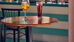 A bar area with two drinks on a wooden table, surrounded by shelves with bottles.