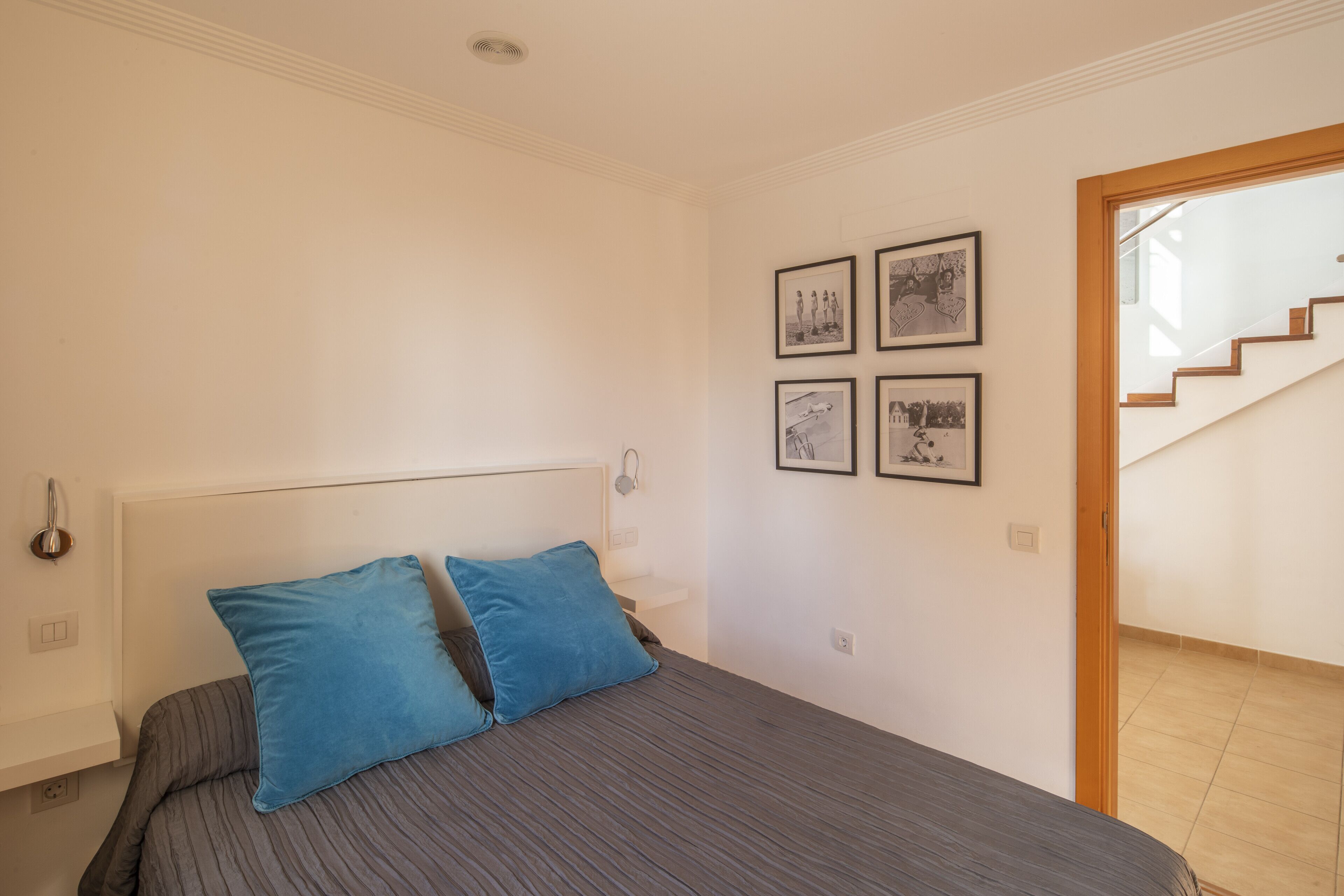 A bedroom with a bed, two pillows, a headboard, and a wall with four framed pictures.