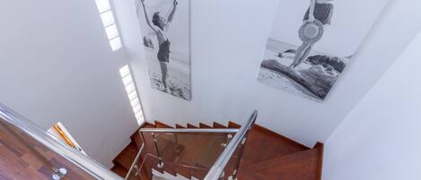 A staircase with wooden steps and metal handrails, leading to a landing with two black and white photographs on the wall.