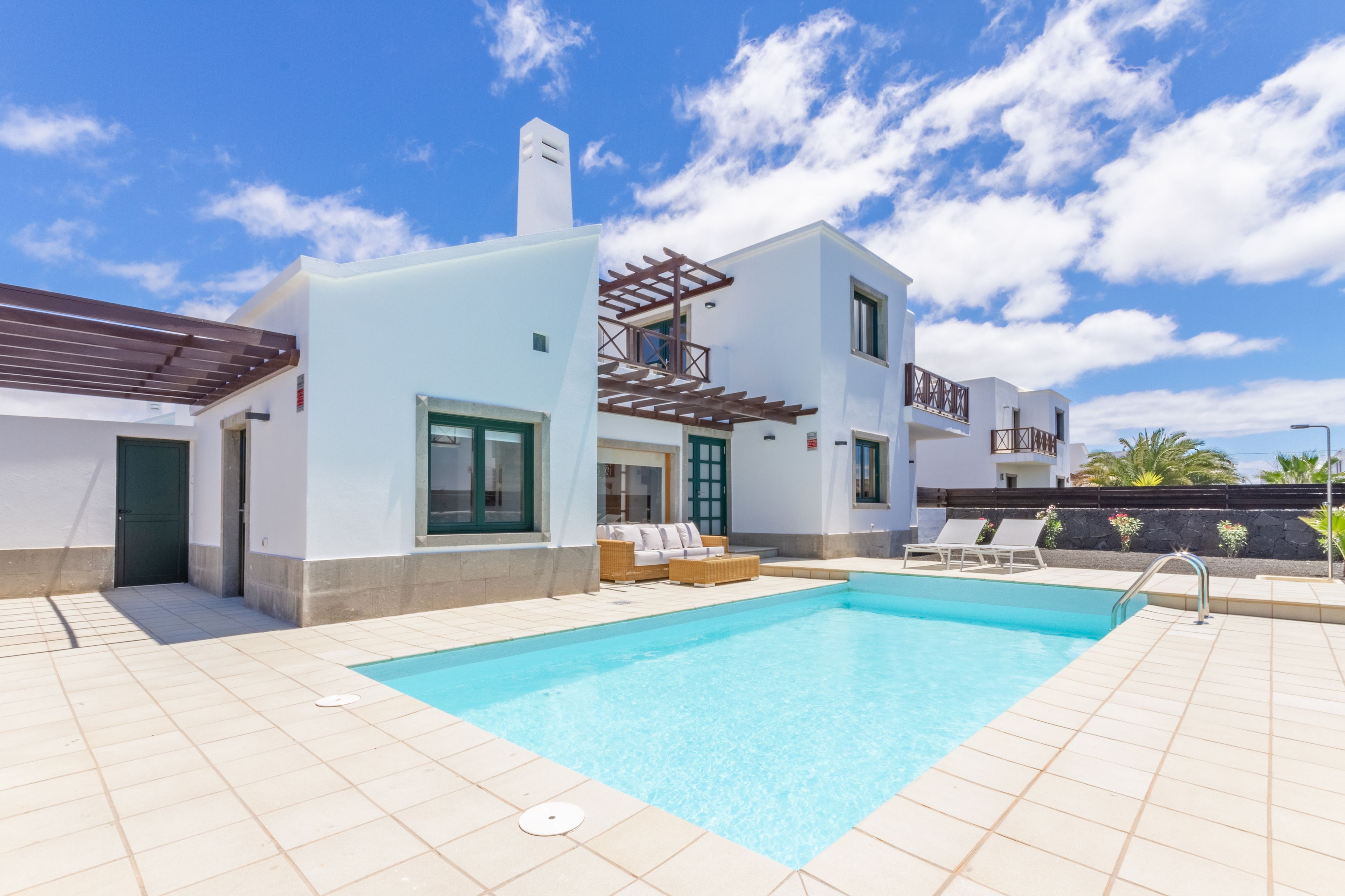 A modern two-story house with a swimming pool, outdoor seating, and a clear blue sky.