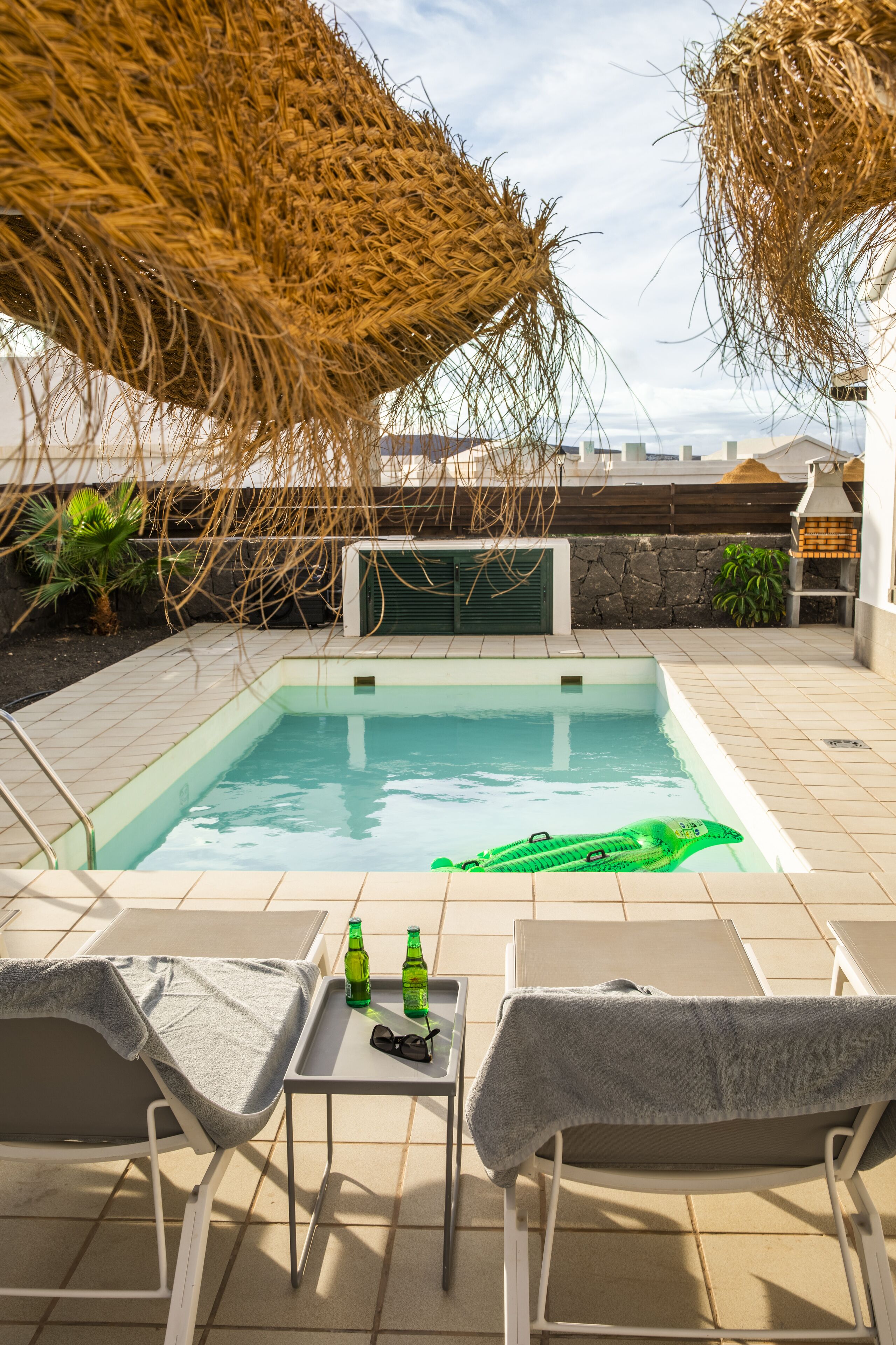 Area piscina con idromassaggio, poltrona relax e tavolo con bottiglie.