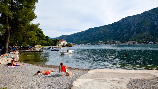 Ein Kiesstrand mit Personen, die sich sonnen, und einem Boot, das in der Nähe der Küste liegt.