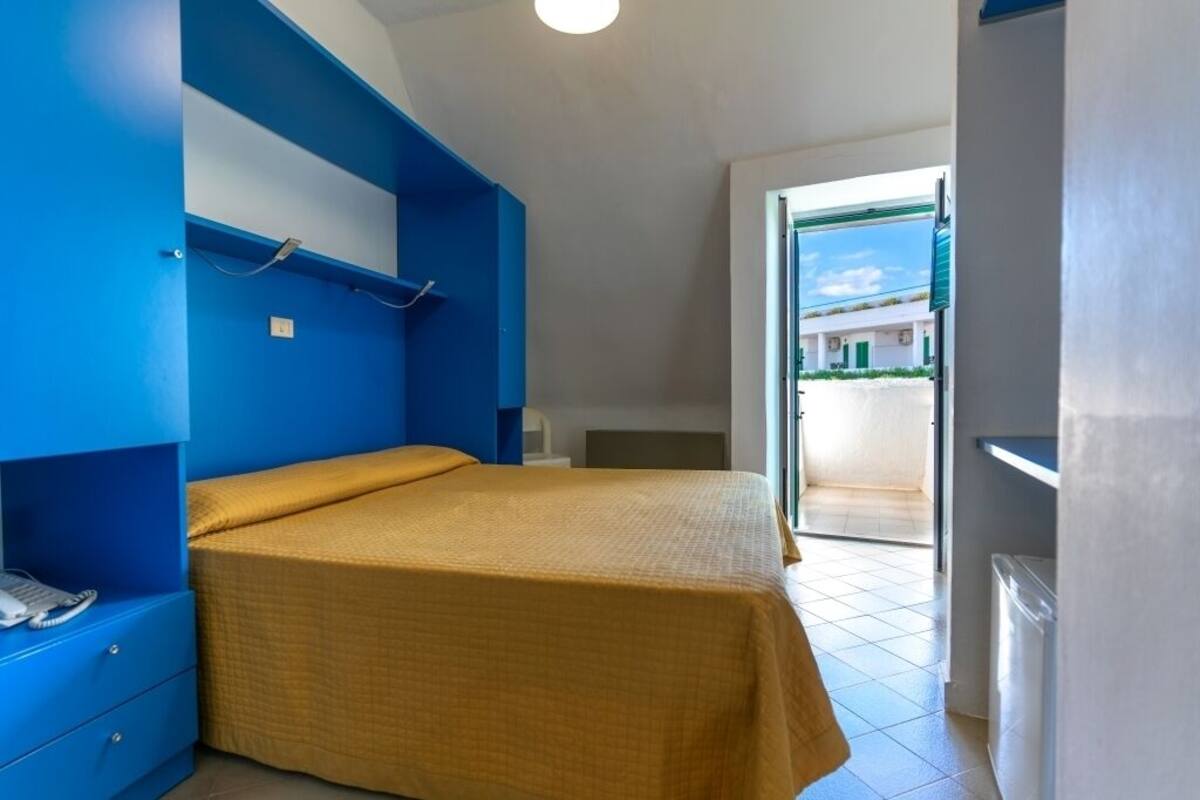 A bedroom with a bed, a nightstand, and a wardrobe. There is a door leading to an outdoor area.