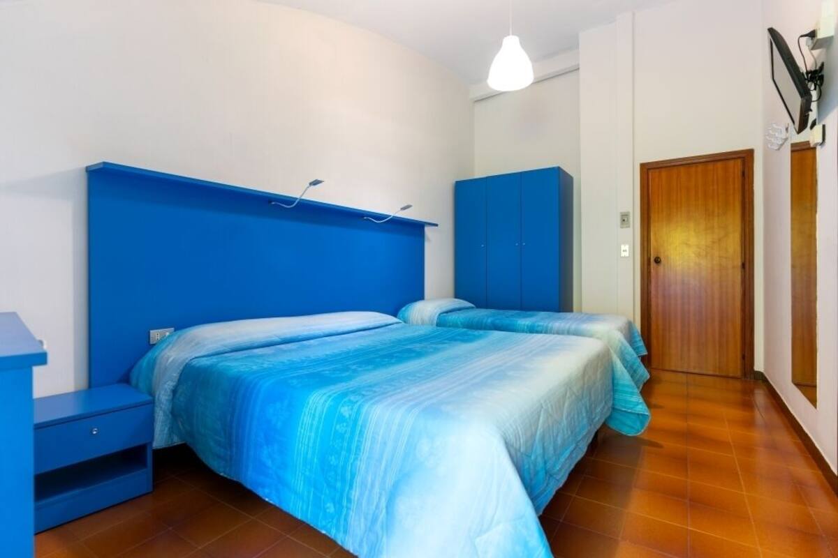 A bedroom with two beds, a blue headboard, a wooden door, and a white wall.