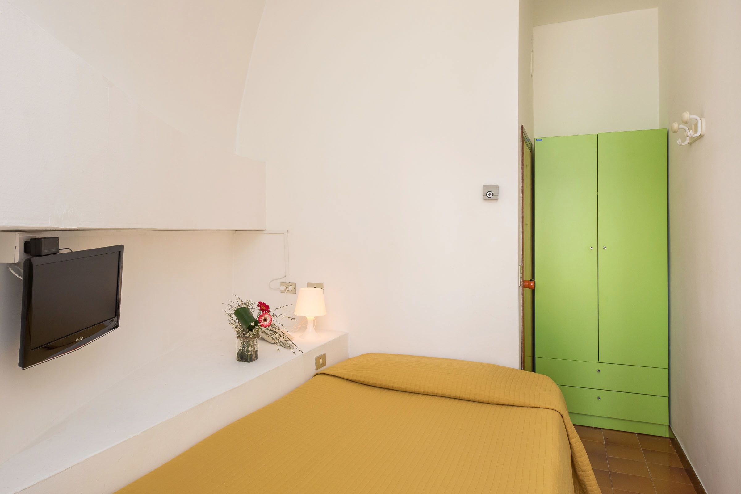 Ein Zimmer mit einem Bett, einem Fernseher, einer Lampe und einem grünen Kleiderschrank.