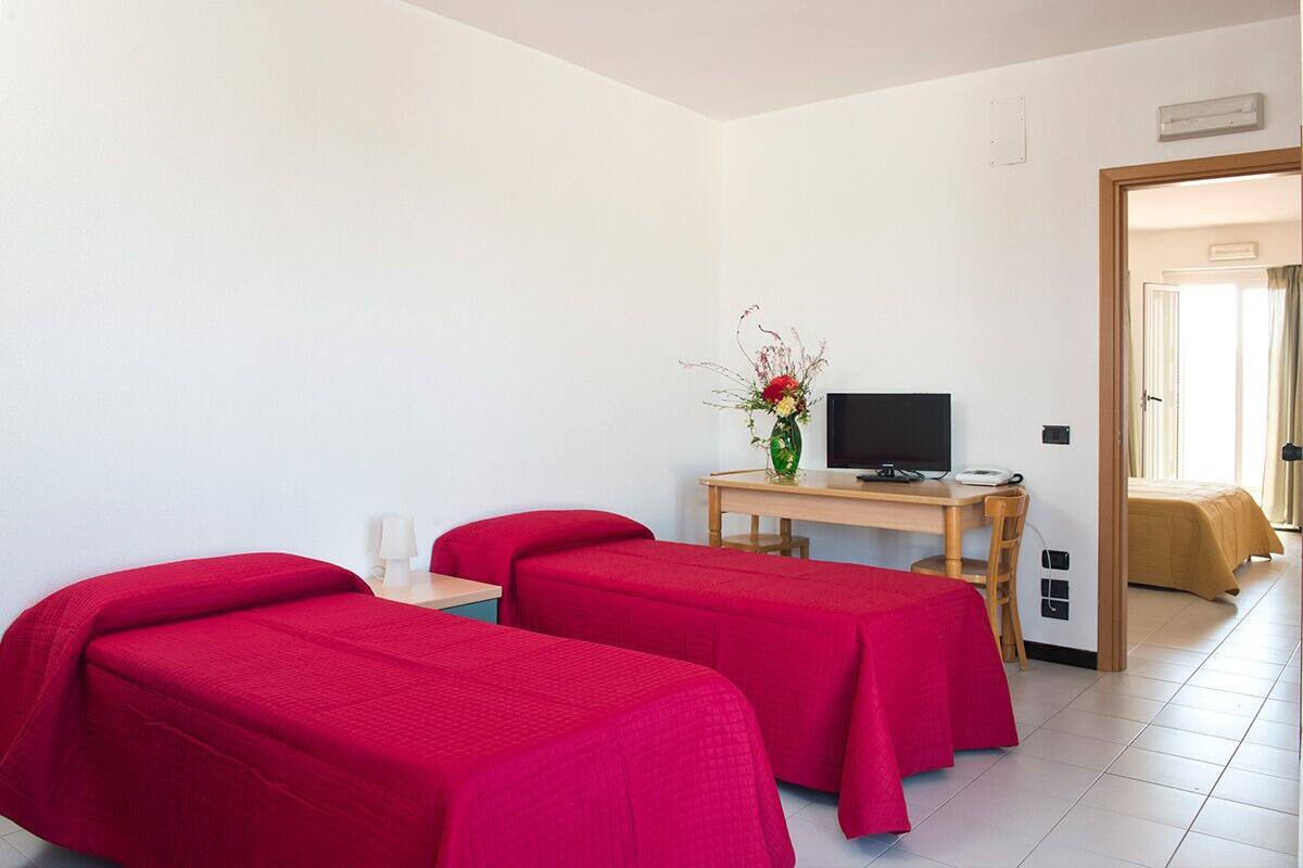 A hotel room with two single beds, a desk with a television, and a small table with a vase of flowers.