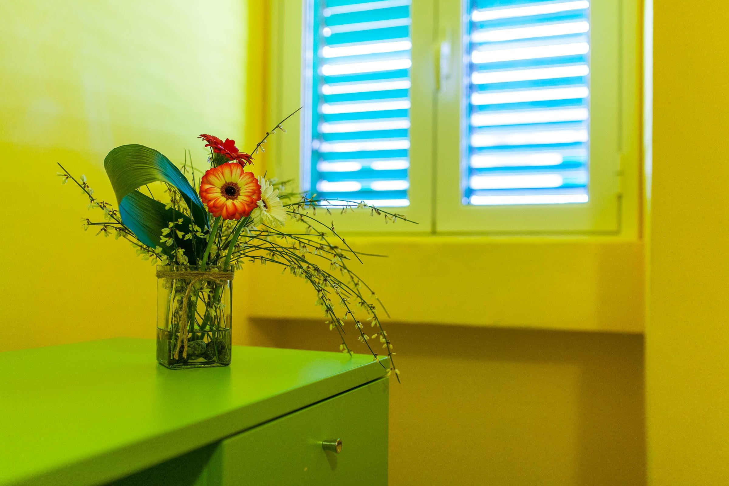 A green desk with a clear glass vase containing flowers and greenery.