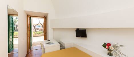 Un dormitorio con cama, escritorio, silla, televisor montado en la pared y ventana con vistas al exterior.