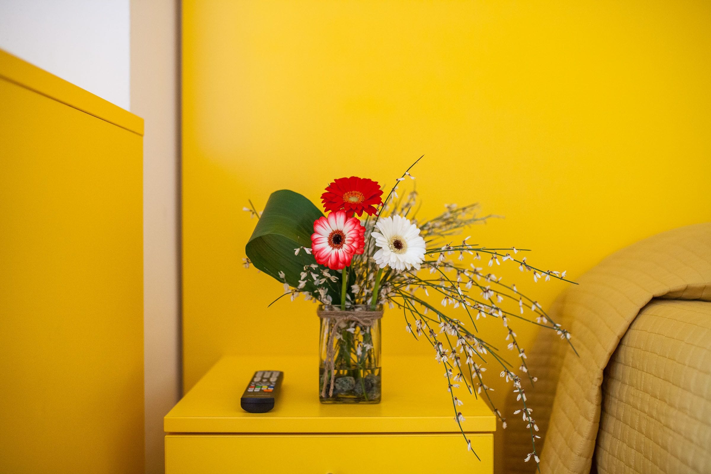 Et gult natbord med en vase blomster og en fjernbetjening.