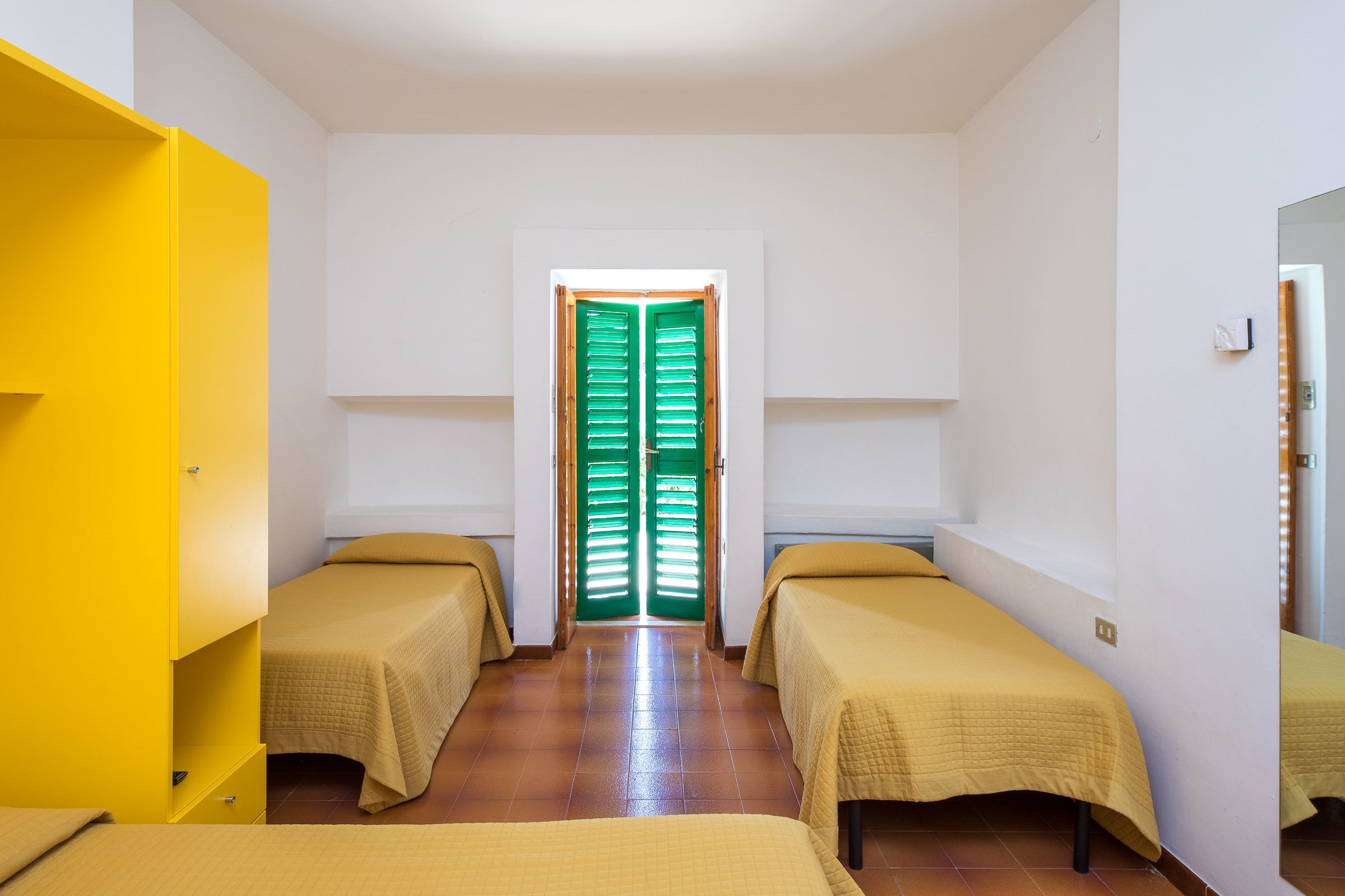 Une chambre avec deux lits simples, une armoire jaune et une porte verte.
