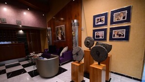 A lobby with a checkered floor, a reception desk, a purple sofa, and stone sculptures on pedestals. - Brazilia Suites Hotel (Baabda)