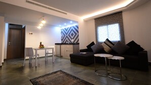 A modern living room with a sofa, two small tables, a dining table with chairs, and a kitchen area with a geometric backsplash. - Brazilia Suites Hotel (Baabda)