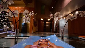 A person lying on a blue lounge chair in a hotel lobby with orchid decorations and a Christmas tree in the background. - Brazilia Suites Hotel (Baabda)